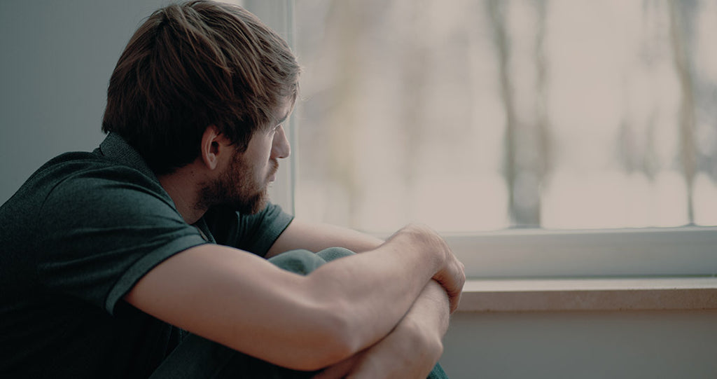 Man looking out window struggling with mental health