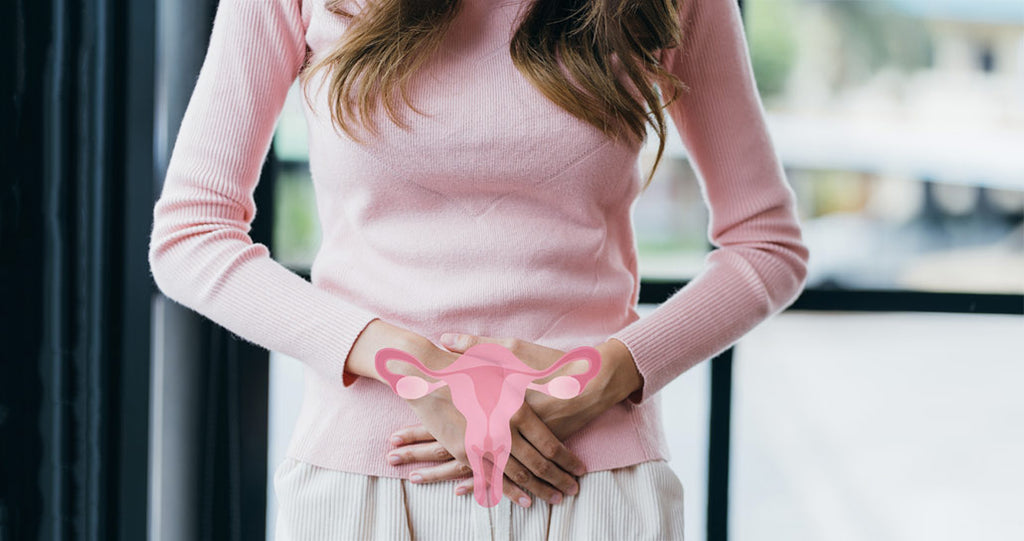 Woman in pink top holding her lower abdomen alluding to PCOS symptoms