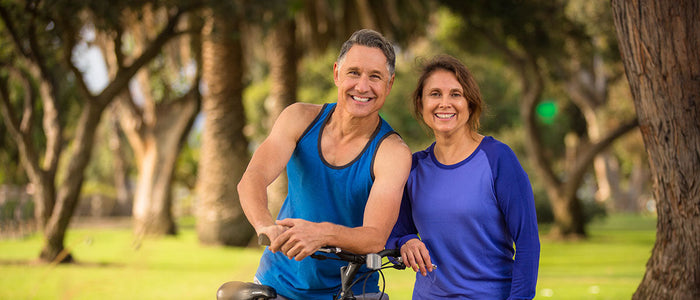 middle aged female and male, smiling and riding a bike at the park