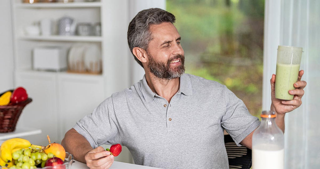 Middle aged man with a smoothie on one hand a fruit on the other