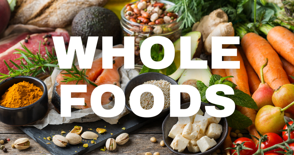 Photo of various fresh produce, spices, tofu, legumes, nuts, and red meat on a kitchen surface. The words "WHOLE FOODS" sit on top of the image.