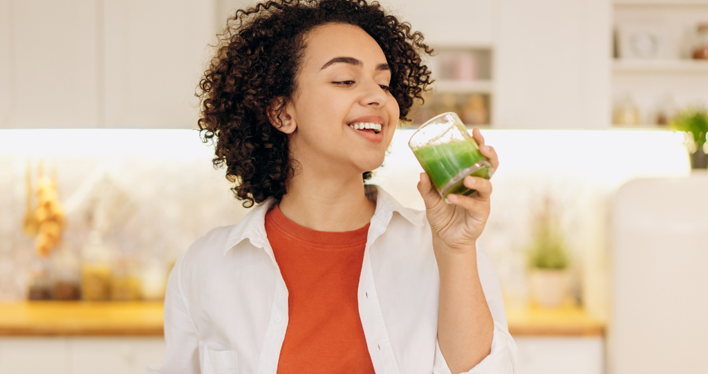 Young woman smiling and drinking a green juice