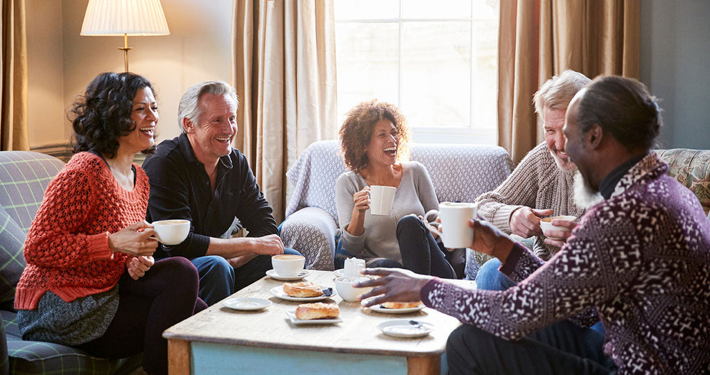 Group of middle-aged friends laughing and drinking tea and coffee