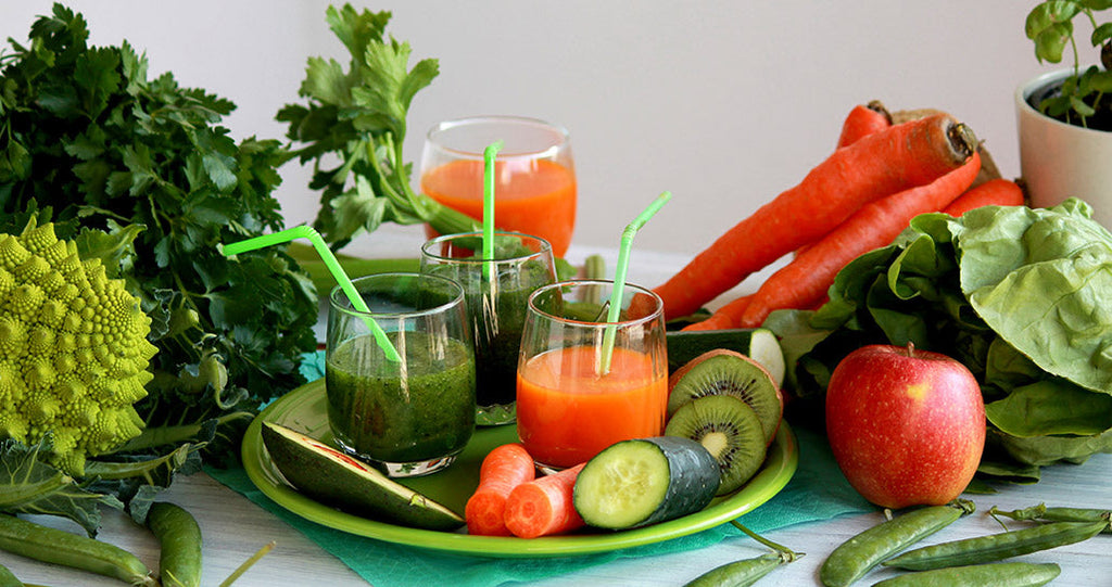 3 colorful smoothies with straws surrounded by various fruits and vegetables