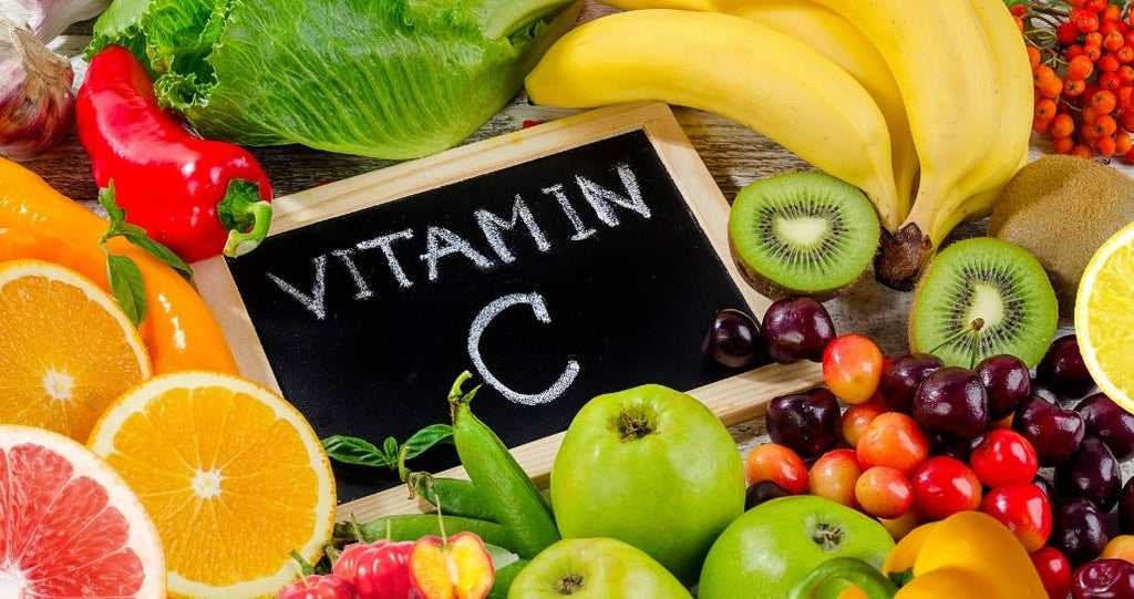 Sign reading vitamin C surrounded by vitamin C-rich foods such as oranges, kiwi, bell peppers, and cherries.