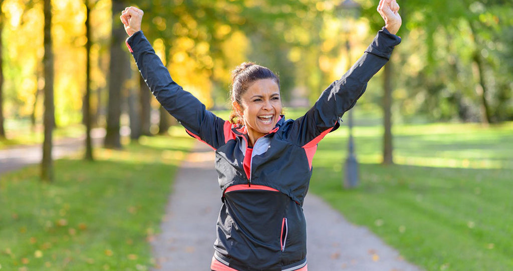 Woman running in the park with arms up in celebration
