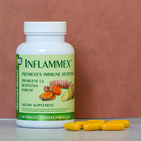 A white bottle of Natura-Genics nflammMex dietary supplement with a green label, shown on a gray surface against a terracotta background, with several yellow capsules in front.