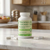 A white bottle of Magnesium Bisglycinate Chelate dietary supplement capsules sits on a white marble kitchen countertop with a few capsules scattered around it. The background shows a softly blurred kitchen interior with wooden cabinets.